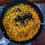 a metal spoon resting in a skillet full of cooked corn