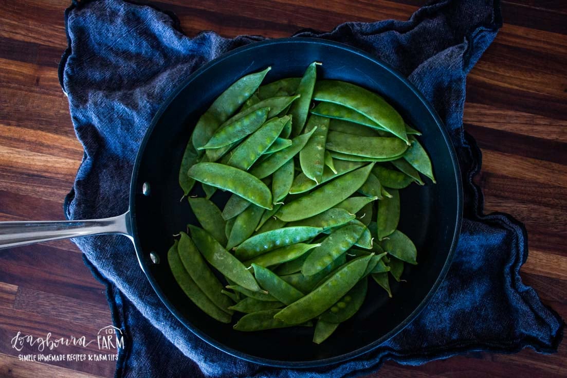 aerial view of a skillet full of green snow peas on a dark blue towel