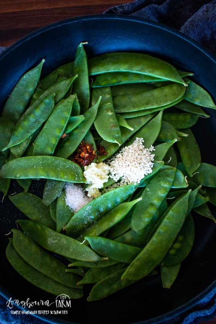 spices on green snow peas in a skillet