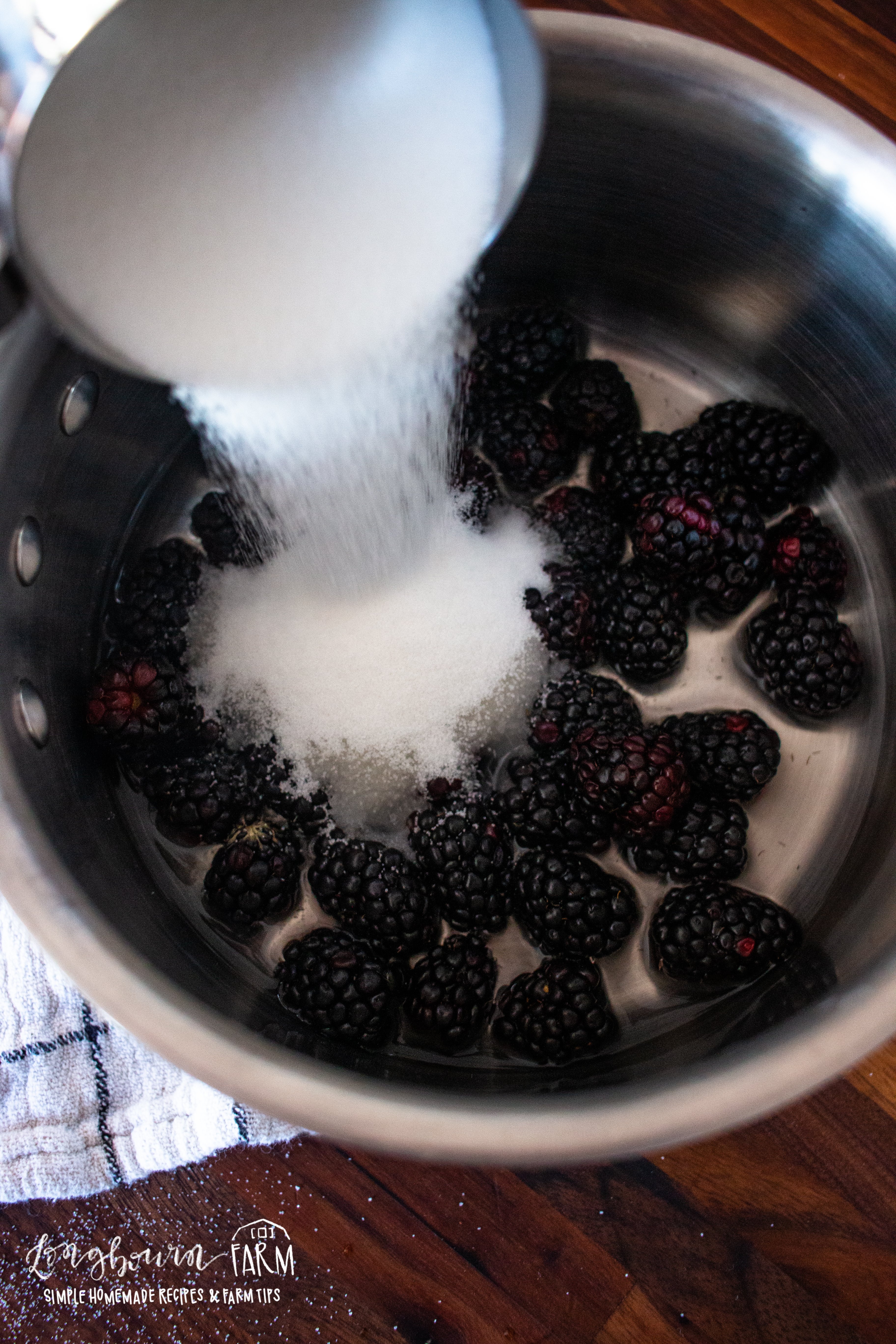 adding sugar to a pot of fresh blackberries
