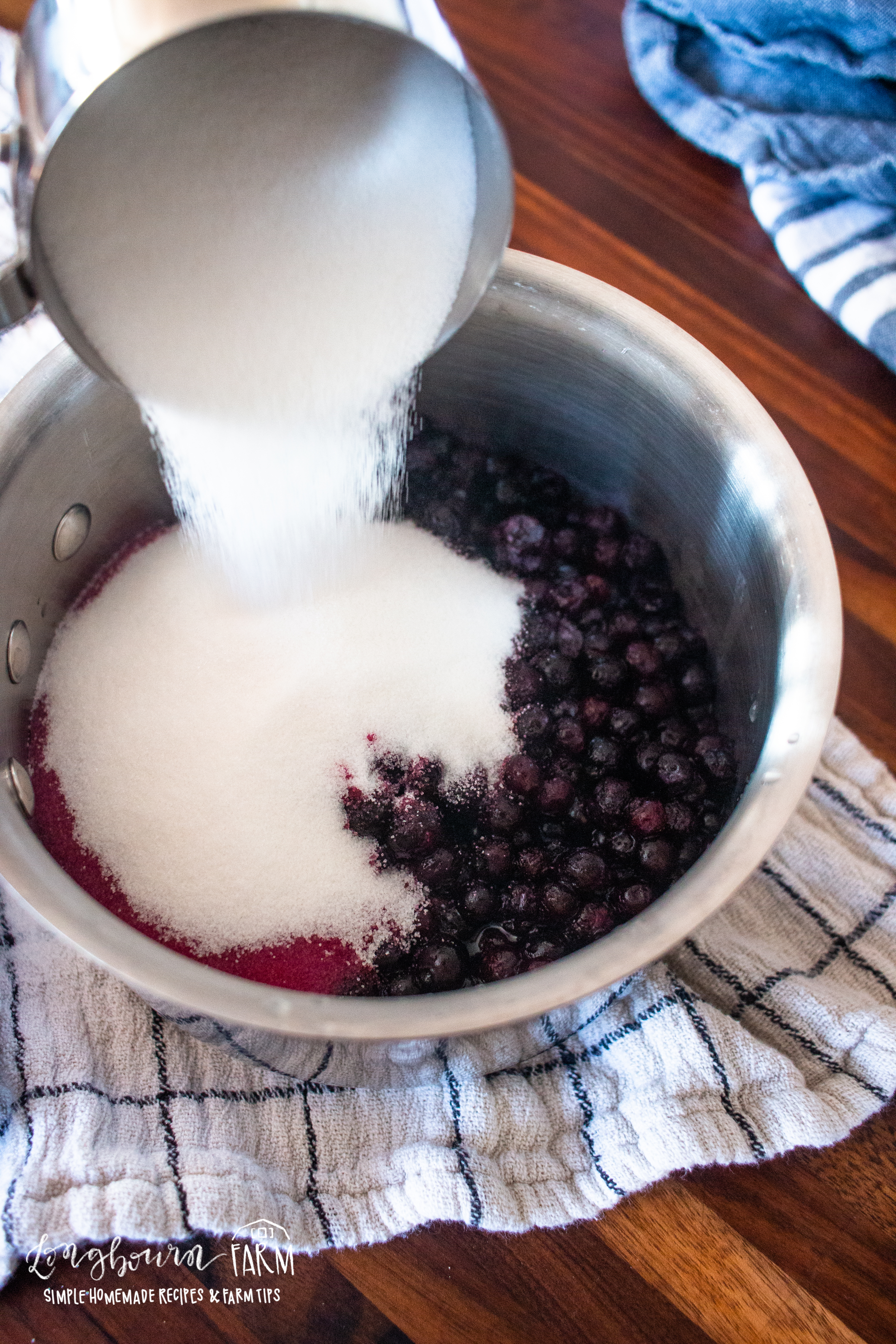 adding sugar to a pot of blueberries