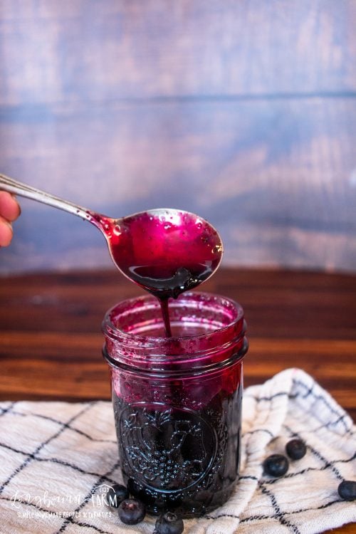 a spoon drizzling blueberry syrup back into a jar of more syrup