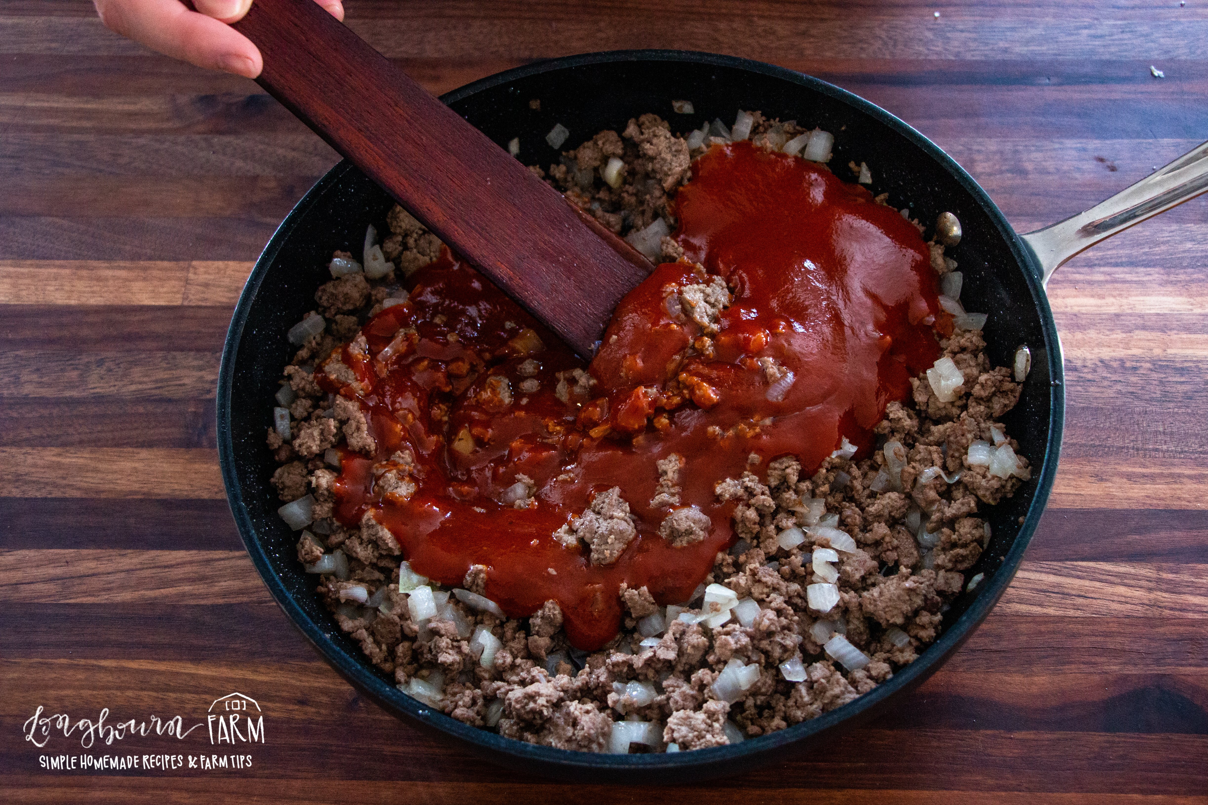 tomato sauce in a skillet full of ground beef and diced onion