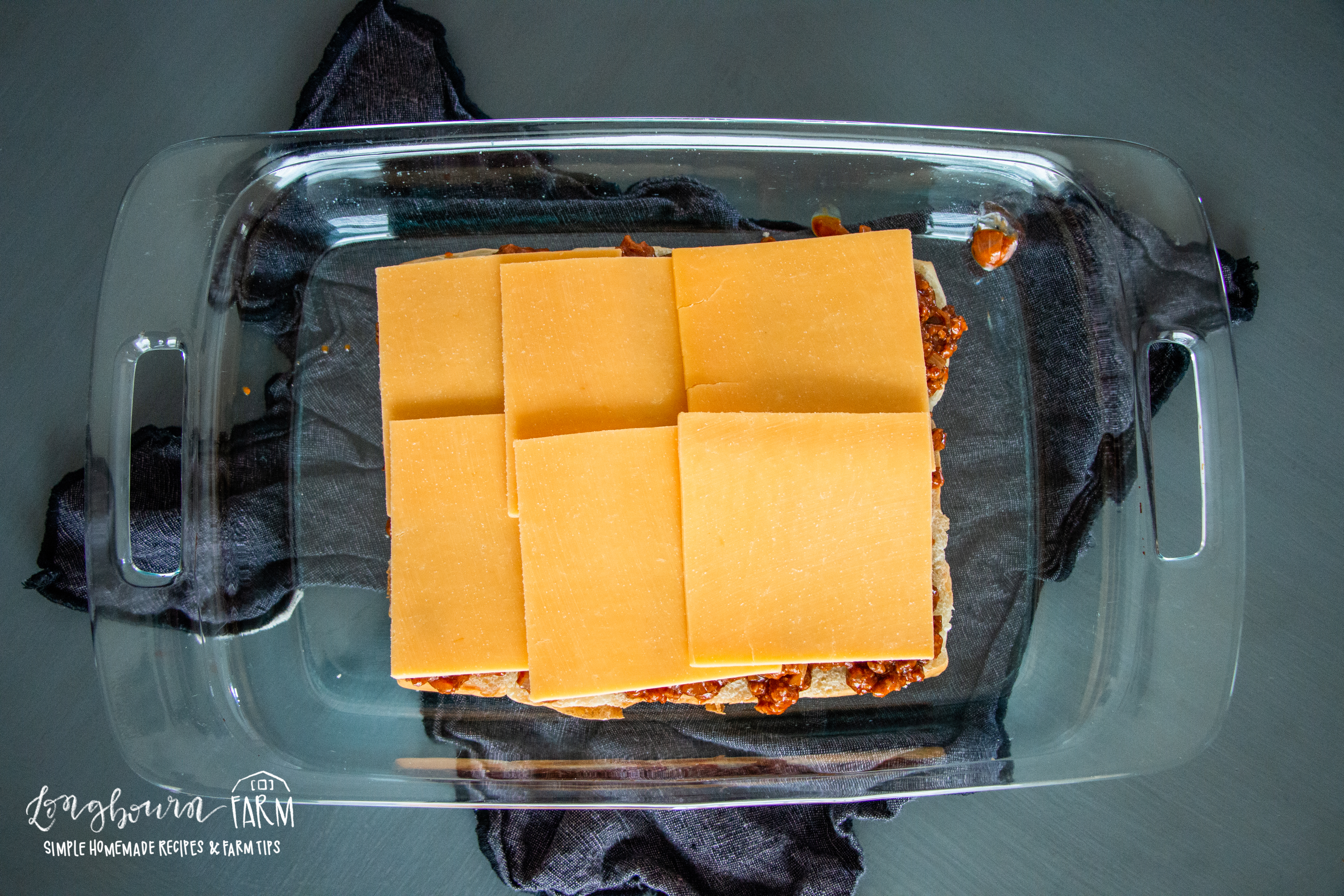 cheese slices on top of bbq beef mixture on sandwich bottoms in a glass baking dish