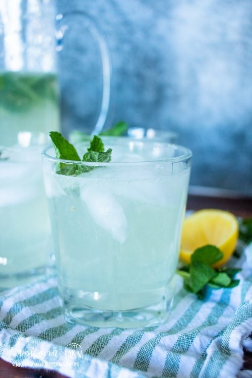a side view of mint lemonade in glass cups with ice and a mint leaf garnish