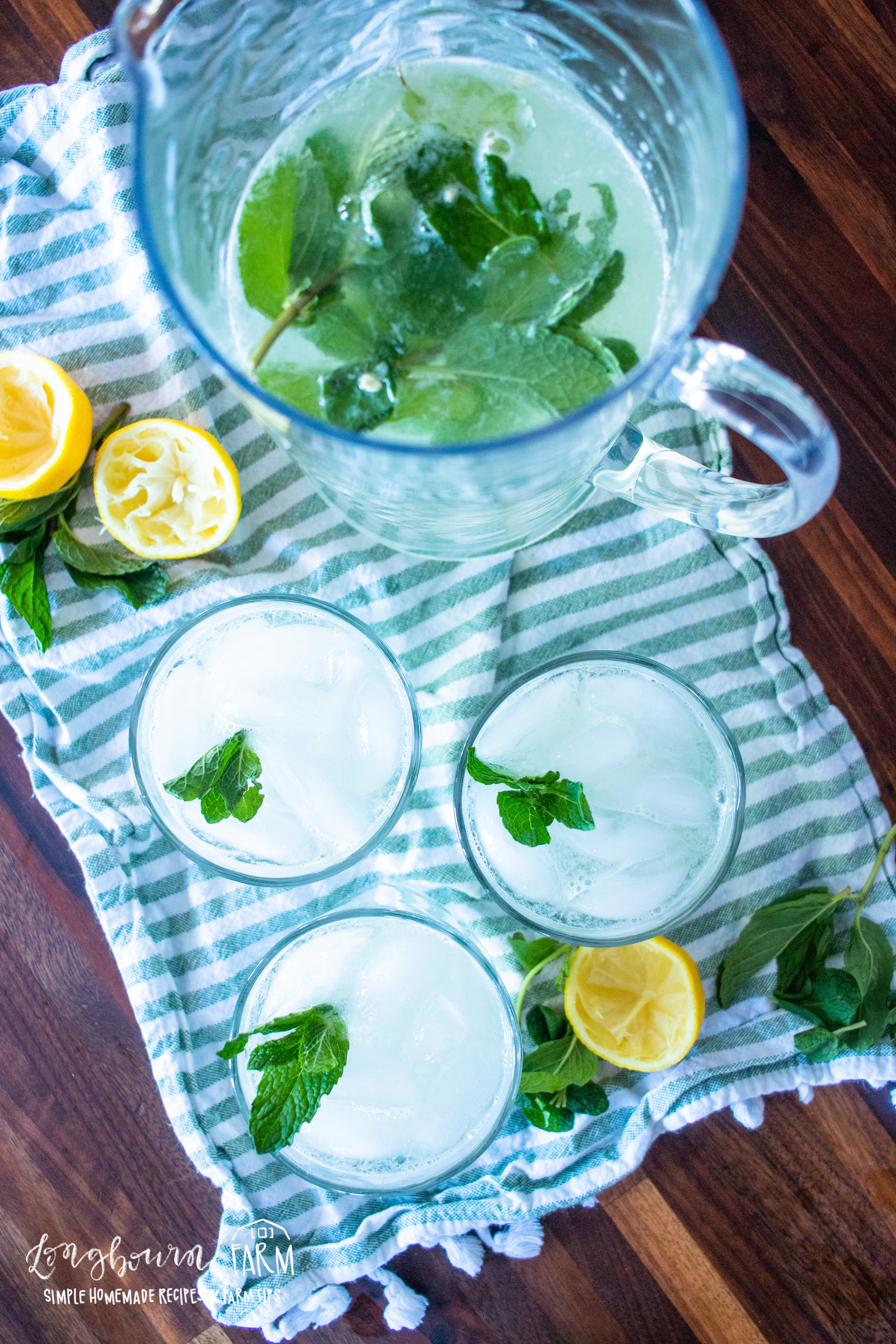 a pitcher and glasses full of mint lemonade with garnish and squeezed lemon halves to the sides