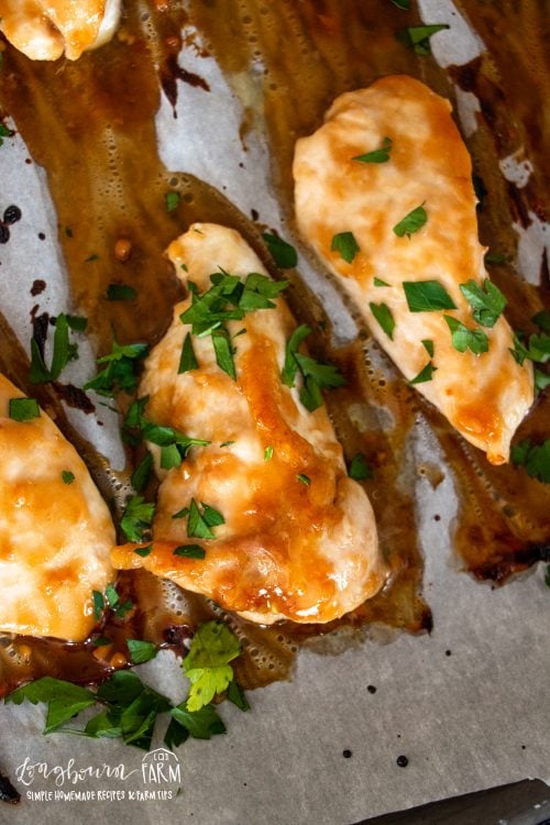 herb topped baked teryiak chicken breasts on a parchment paper lined baking sheet