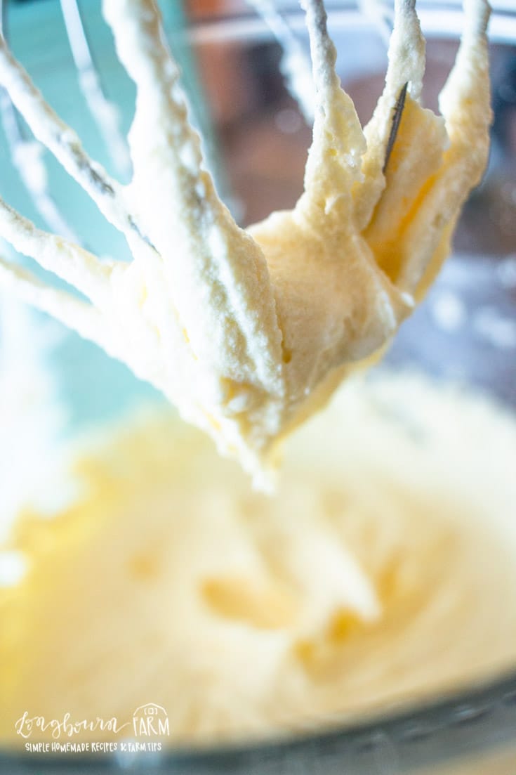 a stand mixer whisk covered in creamed butter and sugar with more in a bowl below