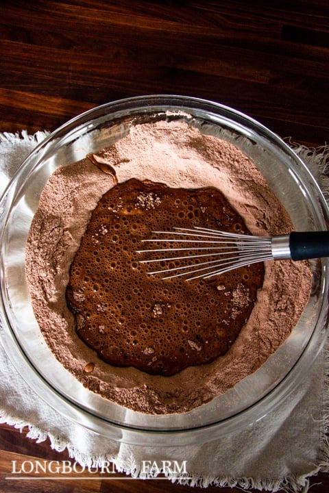 whisking wet ingredients into the chocolate mixture in a glass bowl with a whisk