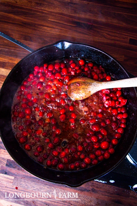 cooking cranberry sauce in a cast iron skillet with a wooden spoon