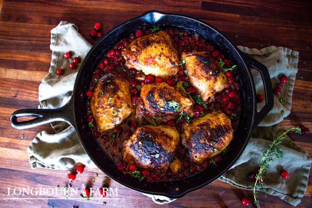 cranberry chciken thighs in a cast iron skillet garnished with fresh chopped herbs
