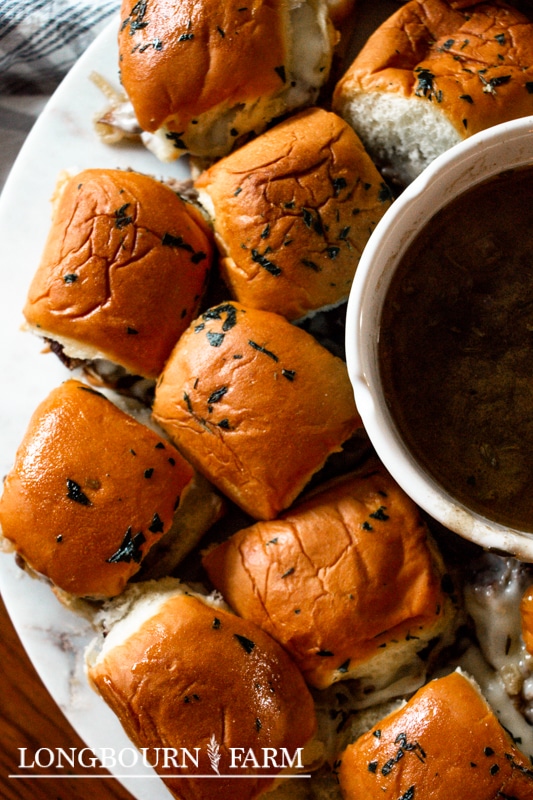 au jus in a bowl next to a bunch of french dip sliders