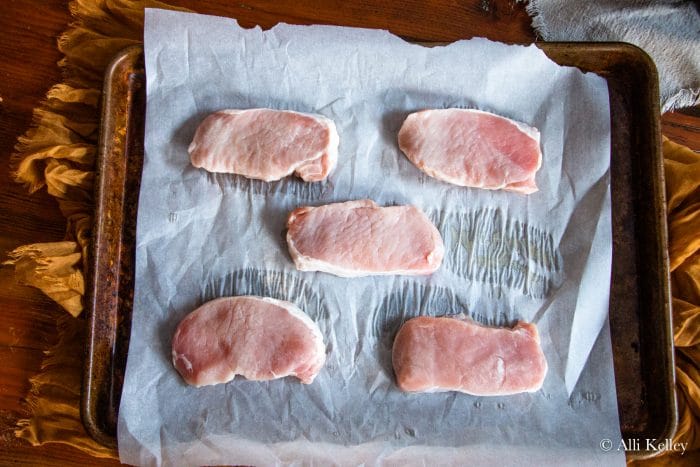 raw pork chops on parchment paper lined baking sheet