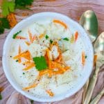 a bowl of instant pot cauliflower soup with shredded carrot, fresh herbs and chopped cauliflower for garnish