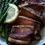 sliced filet mignon wrapped in bacon on a plate with asparagus and a lemon wedge