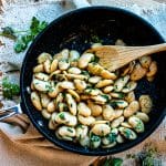 butter beans recipe with herbs in a pan with a wooden spoon