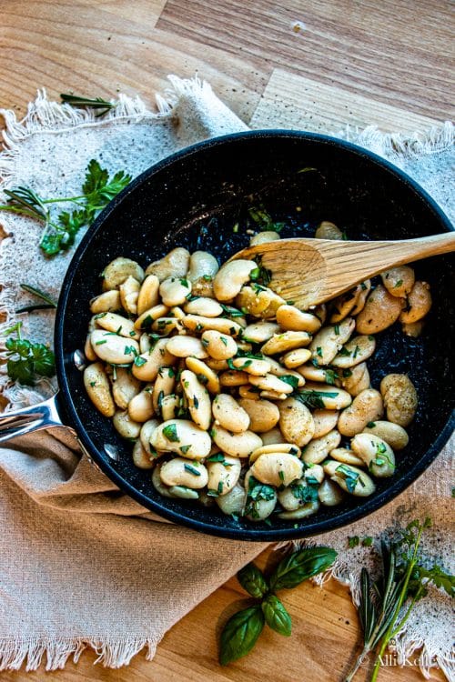 butter beans recipe with herbs in a pan with a wooden spoon