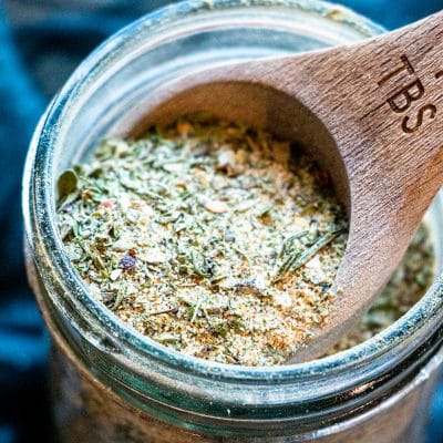 garlic and herb seasoning in a mason jar being scooped with a wooden measuring spoon