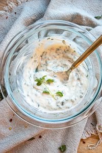 herb aioli in a glass bowl with a spoon and garnished with fresh herbs