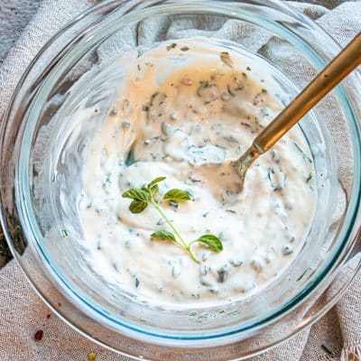 herb aioli in a glass bowl with a spoon and garnished with fresh herbs