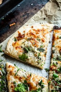a slice of herby garlic cheese bread garnished with fresh herbs on a parchment lined baking sheet