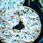 half a bagel covered in herbed cream cheese on a plate