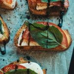 toasted slices of itailian loaf topped with mozzarella, fresh basil and tomatoes drizzled with balsamic glaze on a parchment lined baking sheet