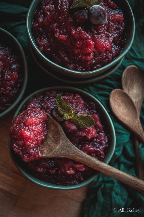 bowls of cranberry apple sauce with a wooden spoon scooping some from one bowl