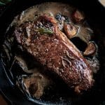 sirloin steak cooking in a pan with melted butter, rosemary and garlic