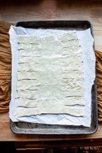 sheet of uncooked puff pastry with the sides sliced into strips on a parchment lined baking sheet