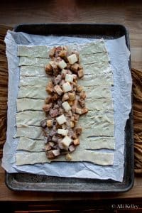sheet of uncooked puff pastry with the sides sliced into strips and apple danish filling down the center, on a parchment lined baking sheet