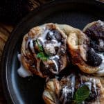 three cherry danish, drizzled with glazed icing and garnished with fresh mint on a black plate