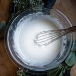 a whisk mixing glazed icing in a glass bowl