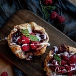 raspberry danish drizzled with glazed icing and garnished with fresh mint leaves on a wooden chopping board