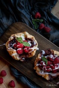 raspberry danish drizzled with glazed icing and garnished with fresh mint leaves on a wooden chopping board