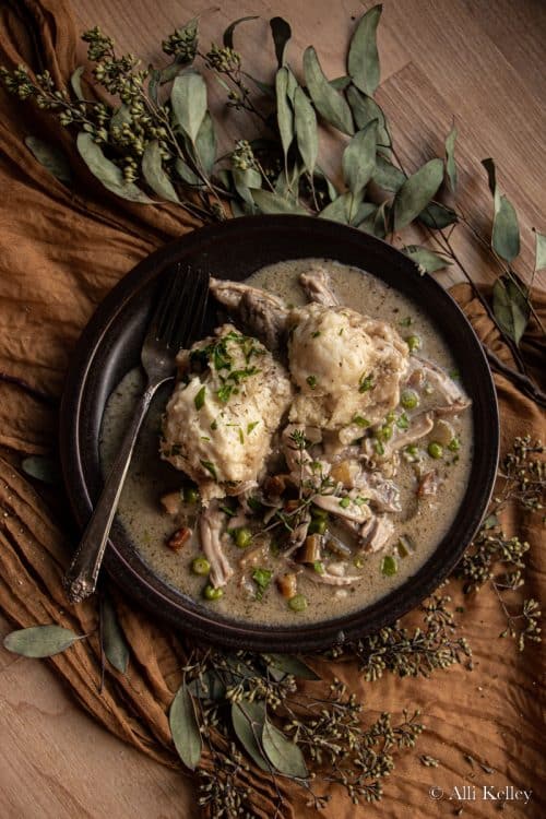 chicken and dumplings garnished with fresh herbs on a black plate with a fork