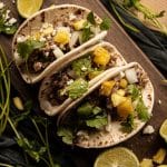 ground pork tacos with chopped pineapple, onions, fresh cilantro and cheese on a wooden chopping board with lime wedges