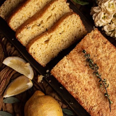 lemon bread with one half cut into slices, garnished with fresh thyme sprigs on a wooden chopping board