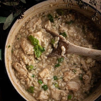 a wooden spoon stirring chicken risotto and fresh herbs in a pan