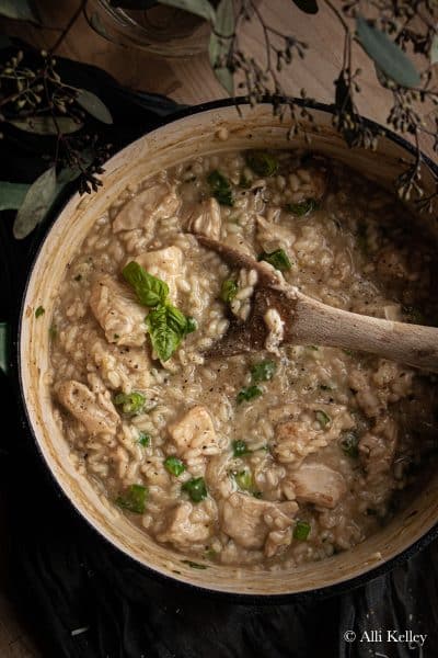 a wooden spoon stirring chicken risotto and fresh herbs in a pan