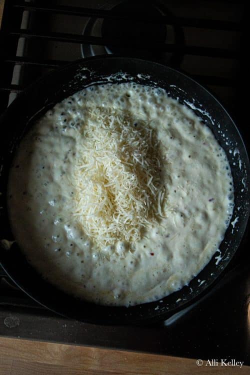bubbling lemon ricotta pasta sauce with grated cheese added on top in a skillet on the stovetop