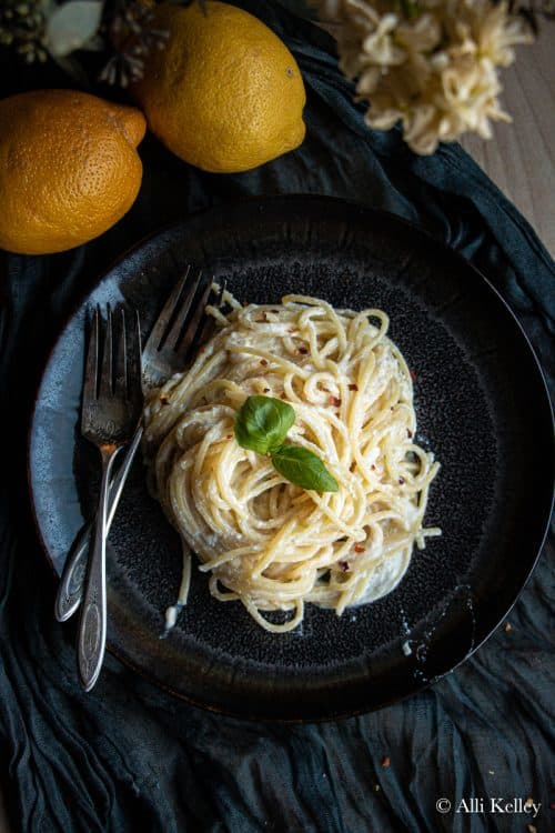 lemon ricotta pasta on a black plate garnished with fresh herbs