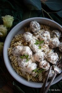 cooked spiral pasta topped with alfredo meatballs and garnished with fresh herbs in a bowl