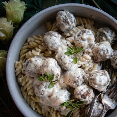 cooked spiral pasta topped with alfredo meatballs and garnished with fresh herbs in a bowl
