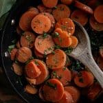 cooked frozen carrots in a pan with fresh herbs and a wooden spoon