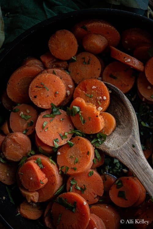 cooked frozen carrots in a pan with fresh herbs and a wooden spoon