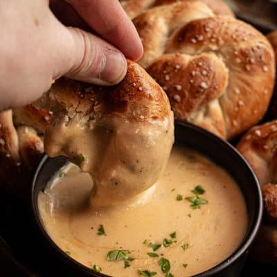 a half eaten pretzel knot being dipped into beer cheese sauce