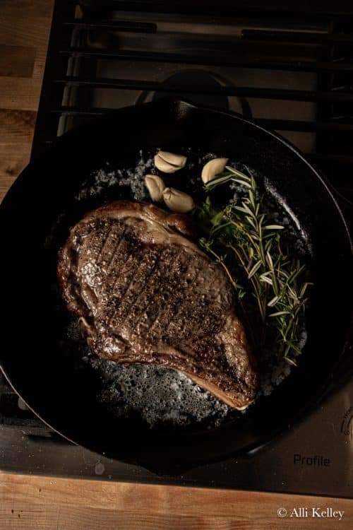 cooked cowboy steak in a pan with fresh herbs and garlic cloves