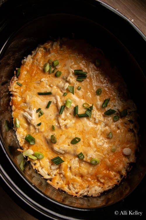 crockpot hashbrown casserole topped with green onions in a slowcooker