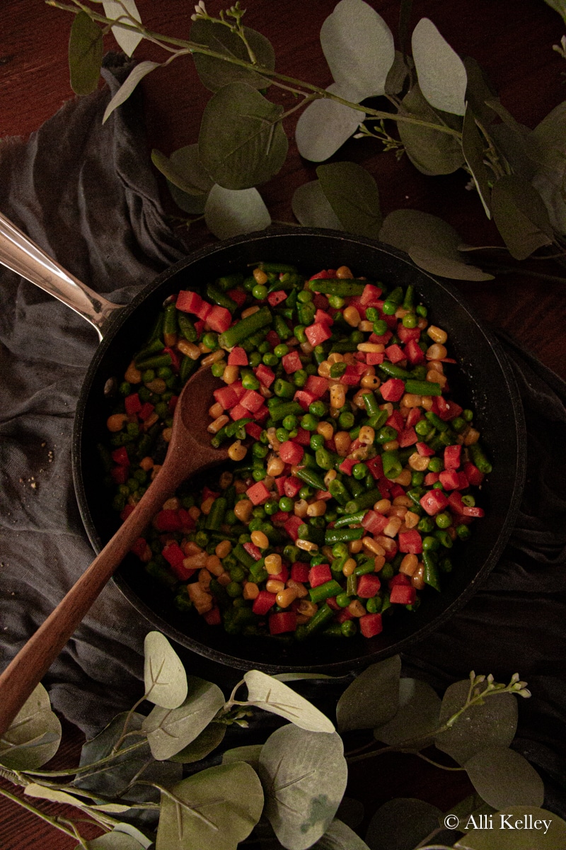 a wooden spoon scooping some veggie medley from a frying pan.